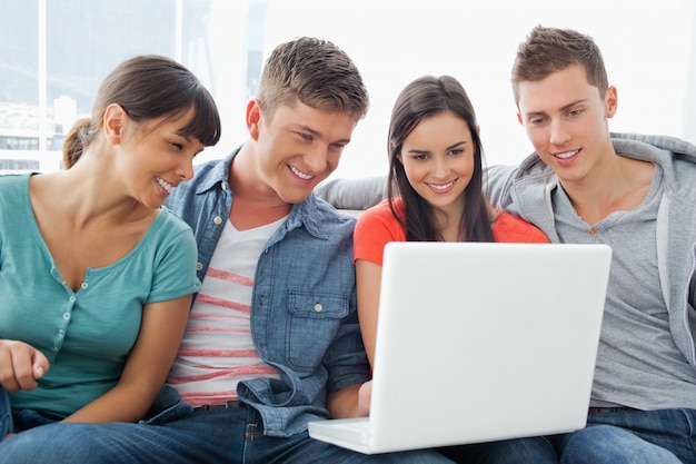 Un sonriente grupo de amigos sentados alrededor de una computadora portátil