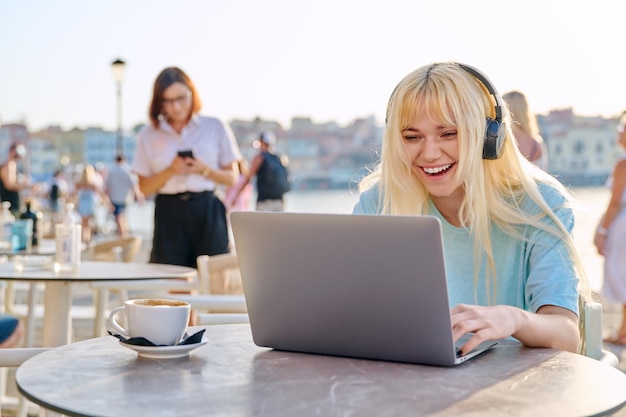 Sonriente hermosa adolescente en auriculares mirando a la computadora portátil