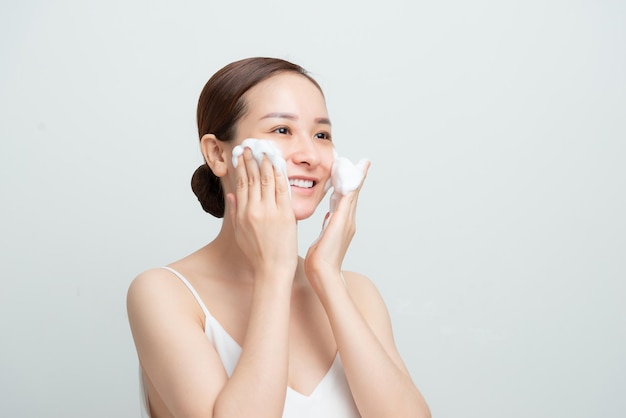 Sonriente hermosa chica asiática usando limpiador espumoso Concepto de lavado de cara aislado sobre fondo blanco