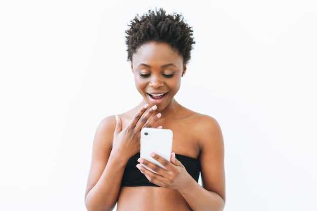 Sonriente hermosa joven mujer afroamericana en top negro usando teléfono móvil aislado