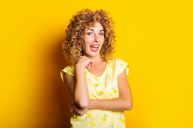 Sonriente a hermosa joven de pelo rizado sobre un fondo amarillo brillante