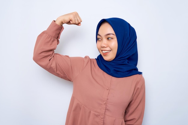 Sonriente hermosa mujer musulmana asiática en camisa rosa levanta los brazos y muestra bíceps demostró su logro después de entrenar en un gimnasio aislado sobre fondo blanco Concepto de estilo de vida religioso de la gente