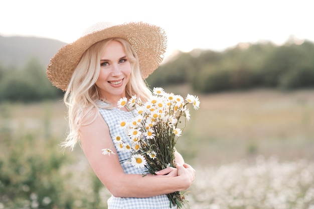 Sonriente a hermosa mujer rubia con ramo de margaritas frescas