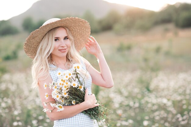 Sonriente a hermosa mujer rubia con ramo de margaritas frescas