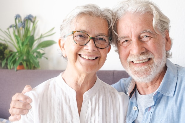 Foto sonriente hermosa pareja senior sentada en el sofá en casa mirando a la cámara