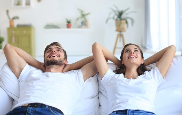 Foto sonriente hermosa pareja sentada en un sofá y soñando con un nuevo hogar.