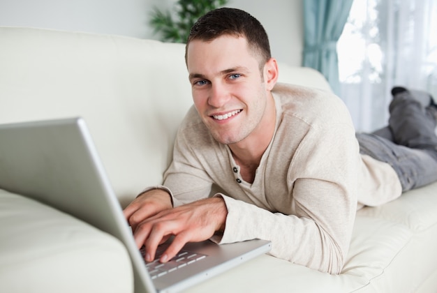 Sonriente hombre acostado en un sofá con una computadora portátil