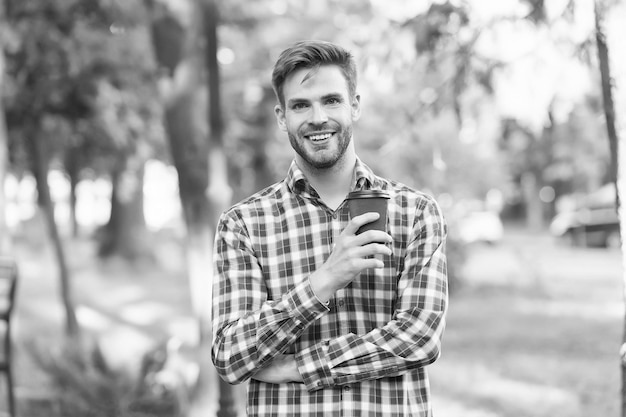 Sonriente hombre sin afeitar bebiendo café matutino en camisa a cuadros inspiración al aire libre