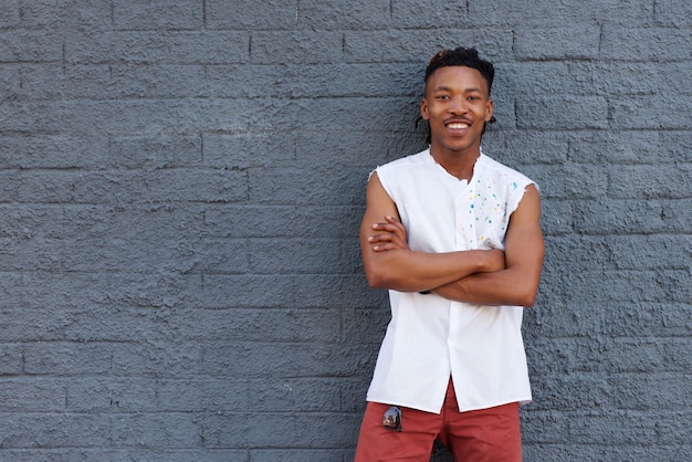 Sonriente hombre africano confía en pie contra la pared gris