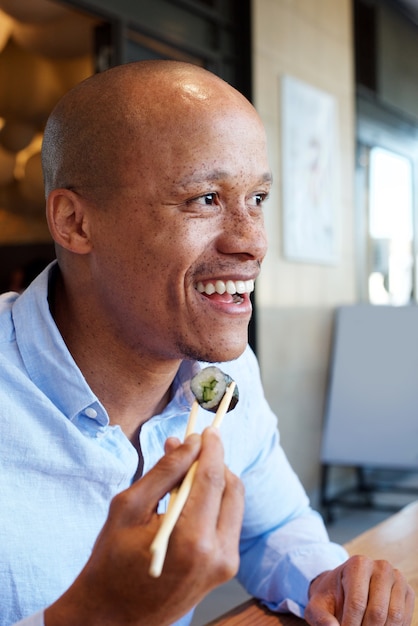 Sonriente hombre africano disfrutando de comer sushi