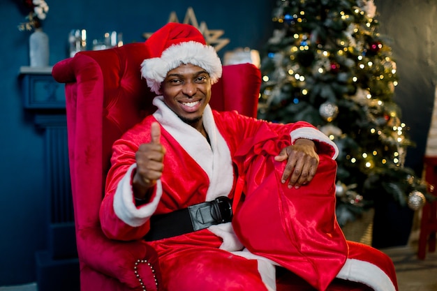 Sonriente hombre africano santa claus sosteniendo un saco rojo con regalos de Navidad