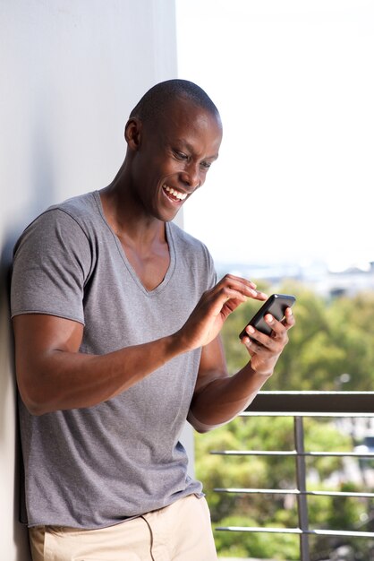 Sonriente hombre afroamericano mirando mensajes de texto en el teléfono