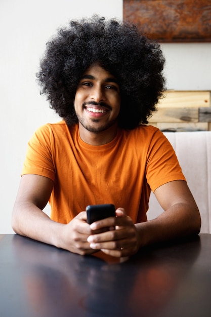 Sonriente hombre afroamericano sentado en casa con teléfono móvil