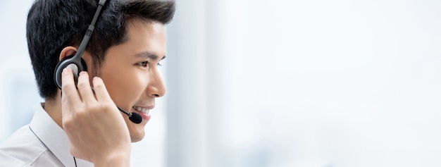 Sonriente hombre asiático guapo con auriculares trabajando en call center como operador de servicio al cliente