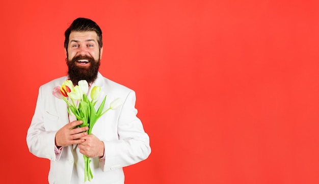 Sonriente hombre barbudo con ramo de flores empresario con ramo de tulipanes para cumpleaños romántico