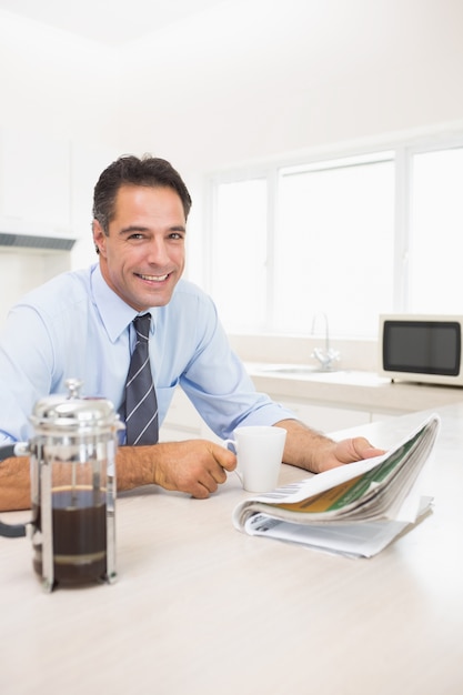 Foto sonriente hombre bien vestido con taza de café y periódico en la cocina