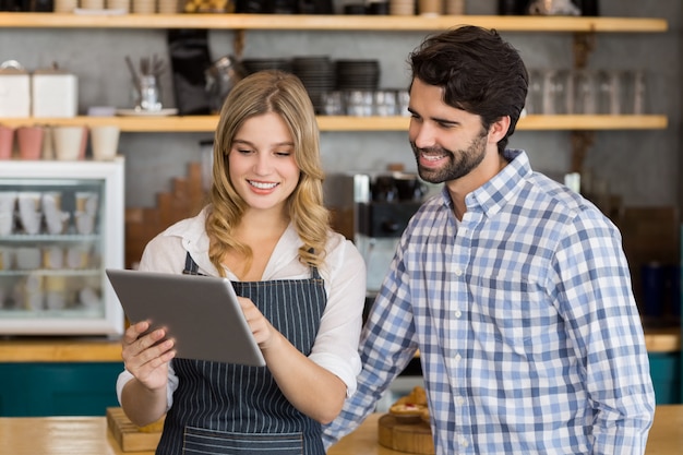 Sonriente hombre y camarera de pie en el mostrador con tableta digital