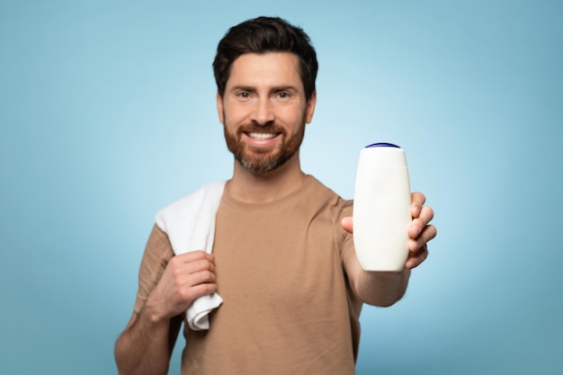 Sonriente hombre caucásico de mediana edad que muestra una botella de champú vacía con maqueta para publicidad de diseño