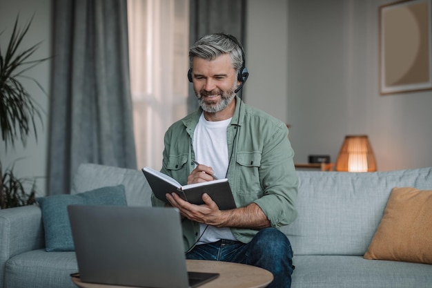 Sonriente hombre europeo de edad feliz con barba en los auriculares se ha reunido de forma remota en la computadora