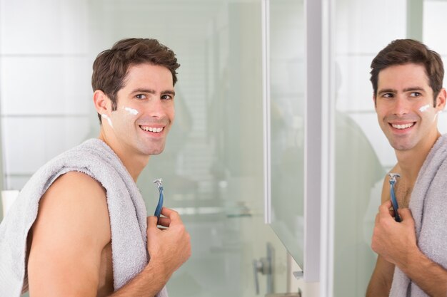 Sonriente hombre guapo con afeitado de reflexión en el baño