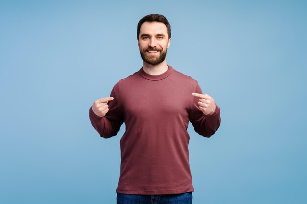 Sonriente hombre guapo barbudo moderno hipster con camisa en blanco señalándose a sí mismo