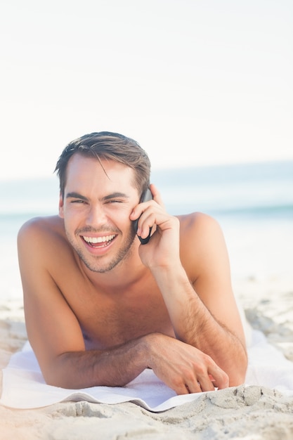 Sonriente hombre guapo en la playa con una llamada telefónica