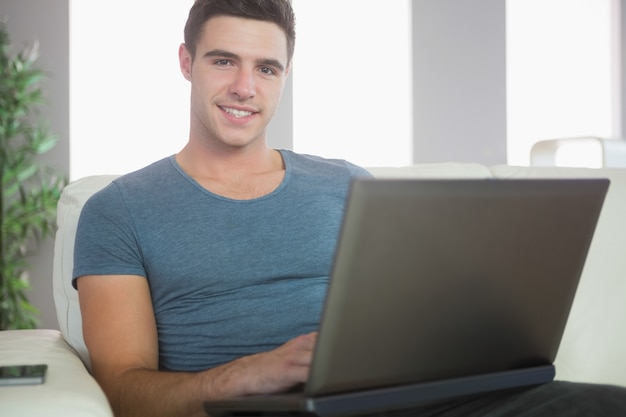 Sonriente hombre guapo de relax en el sofá usando la computadora portátil