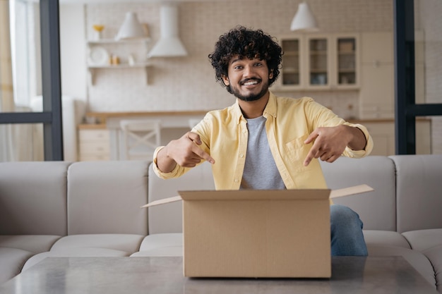 Sonriente hombre indio influyente desempacando caja en casa Concepto de servicio de entrega de compras en línea