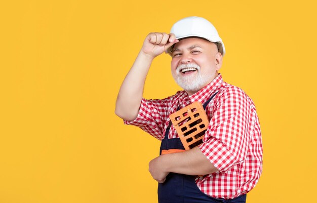 Sonriente hombre mayor albañil en casco sobre fondo amarillo