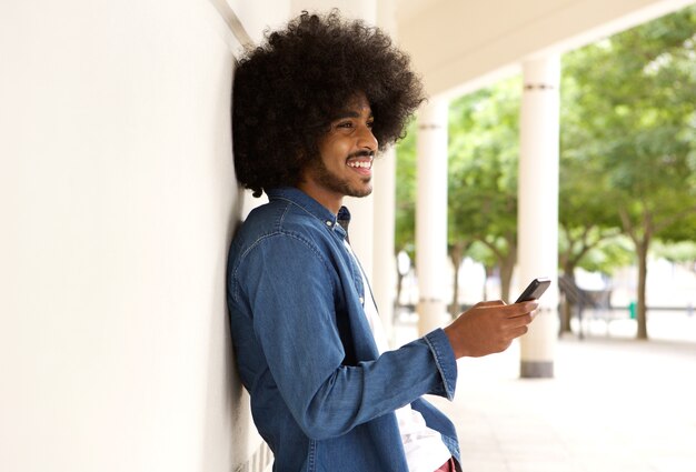 Sonriente hombre moderno parado afuera con teléfono celular