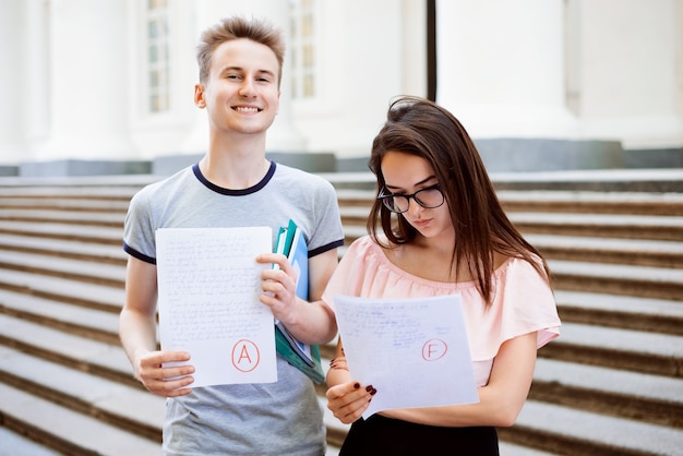 Sonriente hombre y mujer triste con resultados de exámenes cerca de la universidad.