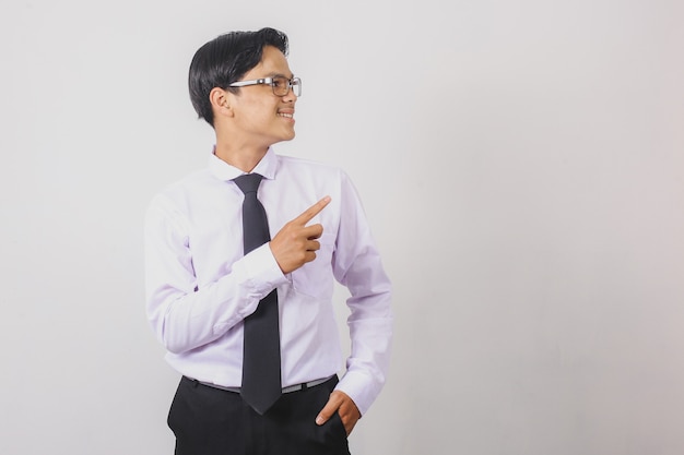 Sonriente hombre de negocios asiático con camisa blanca y corbata negra apuntando al espacio vacío de su lado