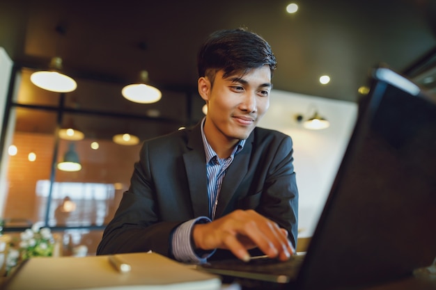 Sonriente hombre de negocios asiático en traje de trabajo con la computadora portátil