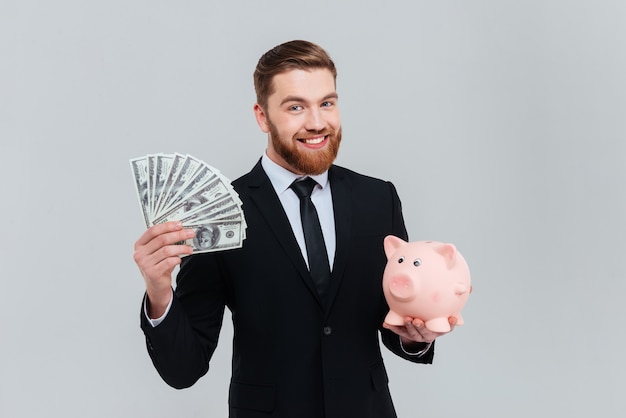 Sonriente hombre de negocios barbudo en traje con caja de dinero y dinero