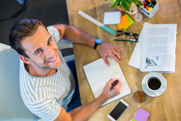 Sonriente hombre de negocios casual escribiendo en Bloc de notas