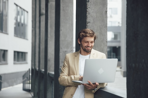 Sonriente hombre de negocios exitoso trabajando en un portátil fuera de la propia oficina