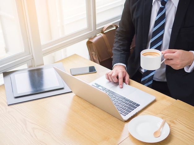 Sonriente hombre de negocios guapo trabajador en vasos bebiendo café en la computadora portátil