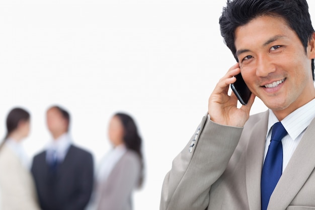 Sonriente hombre de negocios en el teléfono móvil y equipo detrás de él