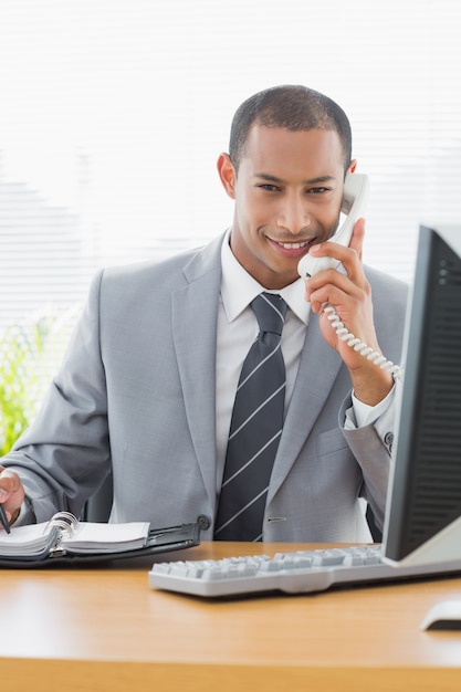 Sonriente hombre de negocios usando la computadora y el teléfono en la oficina
