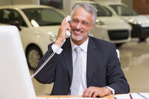 Sonriente hombre de negocios usando el teléfono frente a la computadora