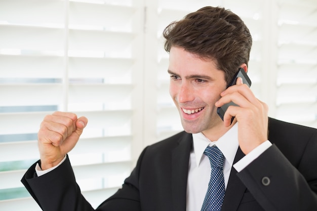 Sonriente hombre de negocios usando el teléfono móvil mientras aprieta el puño