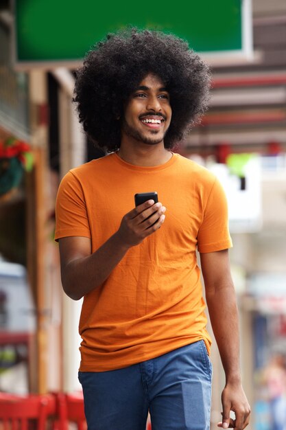 Sonriente hombre negro caminando con teléfono móvil