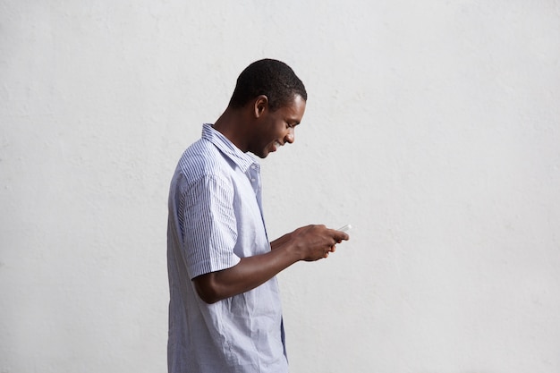 Sonriente hombre negro caminando y usando teléfono móvil