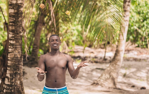 Sonriente hombre negro haciendo malabares con frutas en la playa