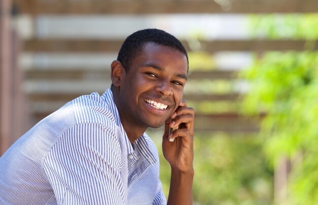 Sonriente hombre negro usando teléfono móvil fuera