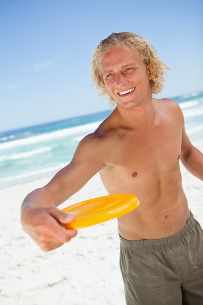 Sonriente hombre rubio de pie mientras juega con un frisbee amarillo