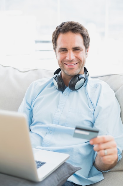 Sonriente hombre sentado en el sofá de compras en línea con la computadora portátil