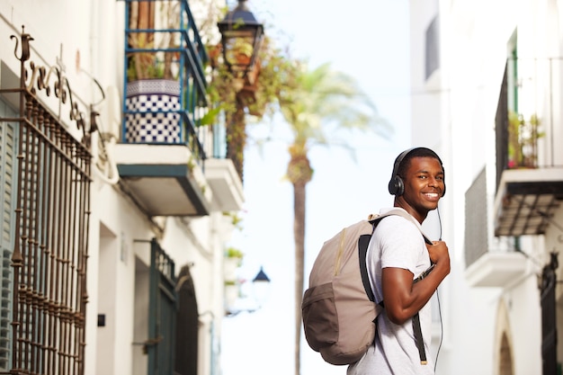 Sonriente hombre de viaje africano con bolsa escuchando música