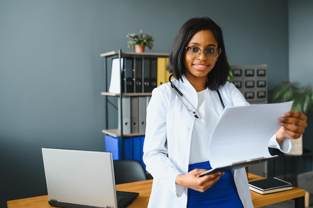 Sonriente joven adulta india doctora usar bata blanca en la oficina de la clínica médica Feliz hermoso cuidado de la salud india profesional médico terapeuta retrato de tiro en la cabeza