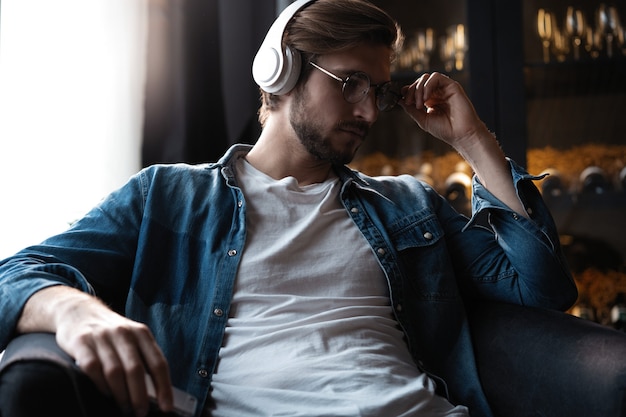 Sonriente joven adulto con audífonos inalámbricos escuchando música móvil en el teléfono inteligente, chico feliz usando el libro de audio de podcast de reproductor en línea en la aplicación en el teléfono celular relajándose en casa